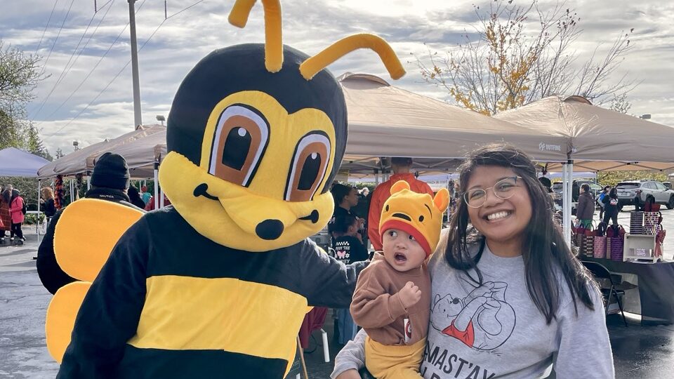 Person in bee costume poses with small child wearing a Pooh costume and their family members.