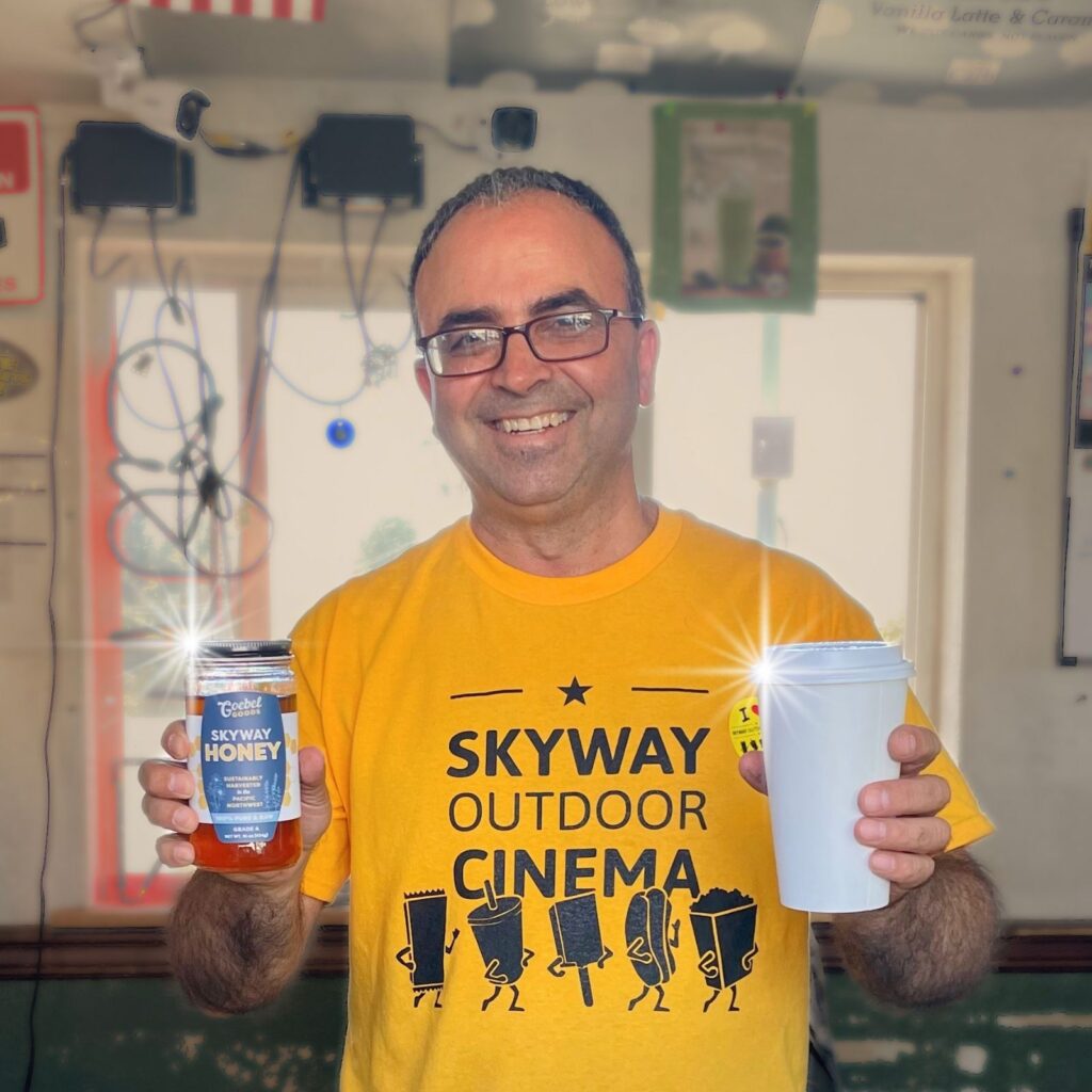 Person holding a coffee cup and a jar of honey.